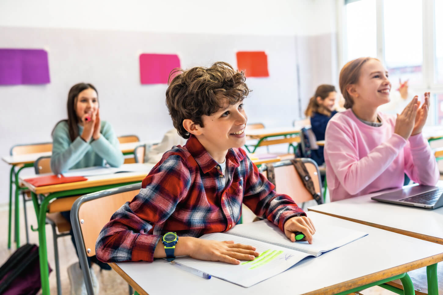 Uśmiechnięte i zaangażowane dzieci siedzą w ławkach w klasie i słuchają swojej nauczycielki angielskiego.